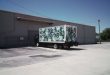 A delivery truck with a floral wrap parked at a warehouse loading dock under a clear blue sky.