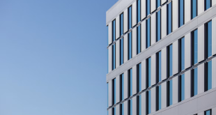 A modern white commercial building with blue-tinted glass windows against a clear blue sky.