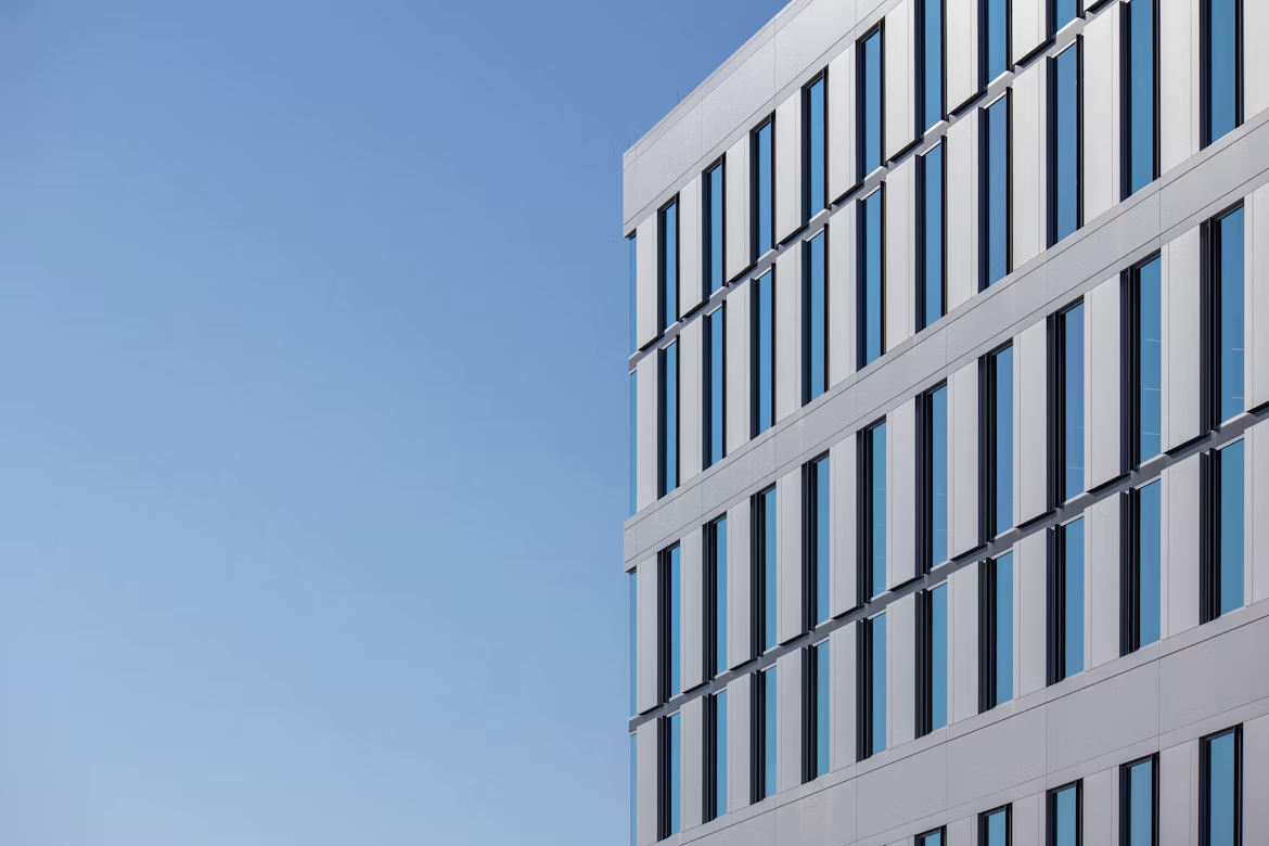 A modern white commercial building with blue-tinted glass windows against a clear blue sky