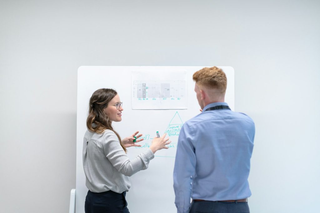 A woman explaining a strategy diagram on a whiteboard to a colleague